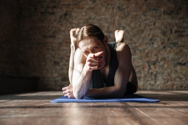 Cheerful strong sportsman in gym lies on floor and pointing