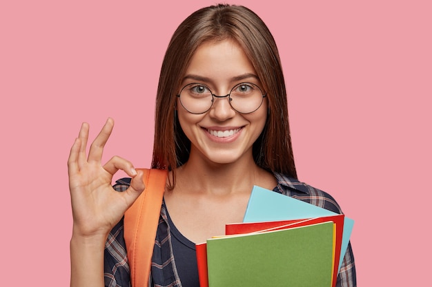 Free photo cheerful student posing against the pink wall with glasses