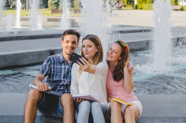 Cheerful students with books taking selfie