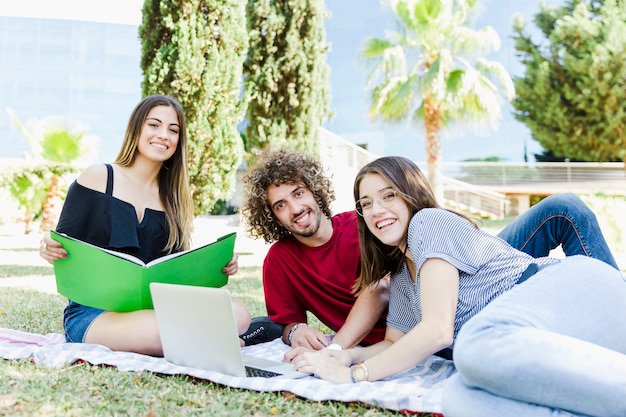 Cheerful students with textbook and modern laptop