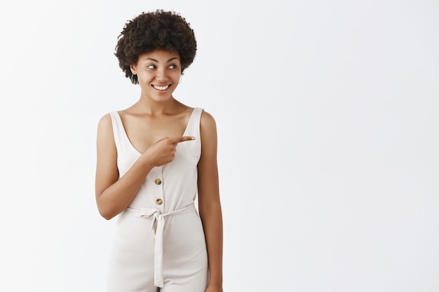 Ragazza alla moda allegra che posa contro il muro bianco