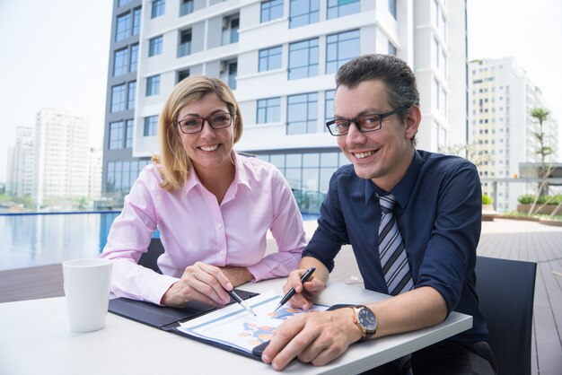 Cheerful successful business team working on report and looking at camera.