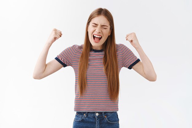 Cheerful successful goodlooking girl in striped tshirt made dreams come true finally achieve goal fist pump raising hands in triumph yelling delighted accomplish victory feeling like champion