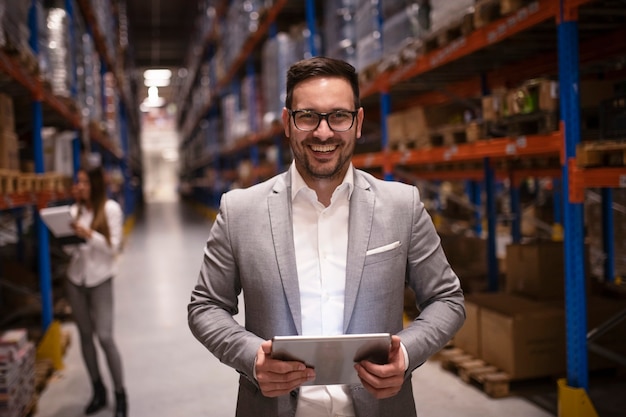 Cheerful and successful middle aged manager businessman holding tablet computer in large warehouse organizing distribution