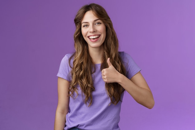 Бесплатное фото Веселая, поддерживающая жизнерадостная общительная кавказская девушка, как ваша идея, положительное мнение, одобрение, показывает палец вверх, удовлетворенная улыбка, широкое принятие, отличный план, стоять на фиолетовом фоне