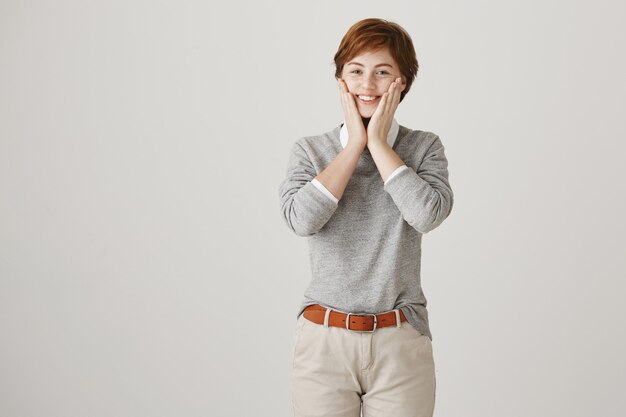 Cheerful surprised redhead girl with short haircut posing against the white wall