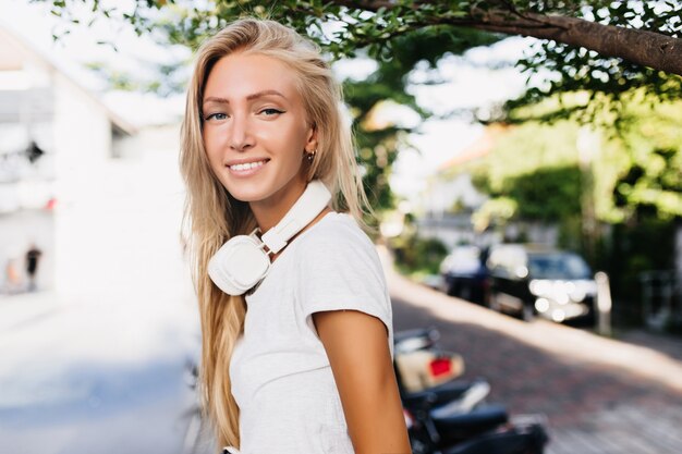 Cheerful tanned lady in headphones spending time outdoor in warm sunny day.