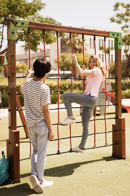 Cheerful teen friends on climbing net on playground 
