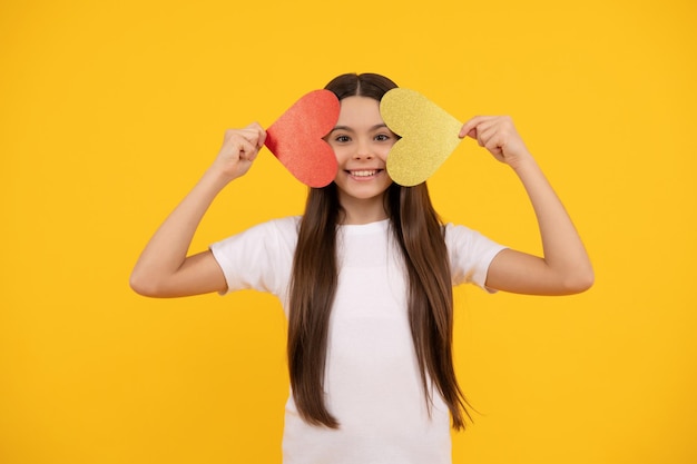 Cheerful teen girl holding valentines heart on yellow background, sweetheart