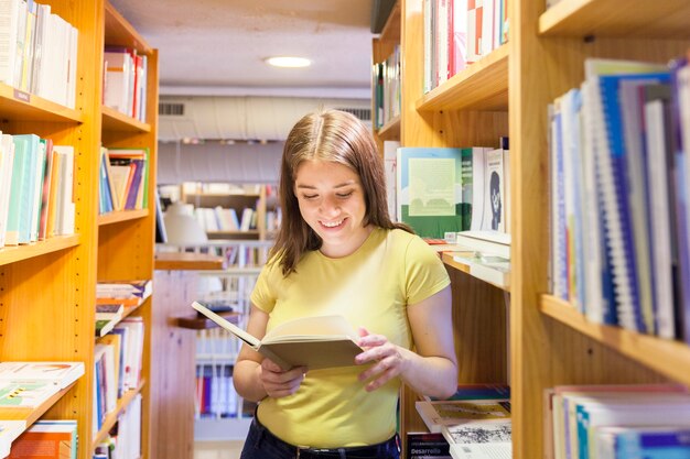 Веселая девочка-подросток, читающая между книжными шкафами