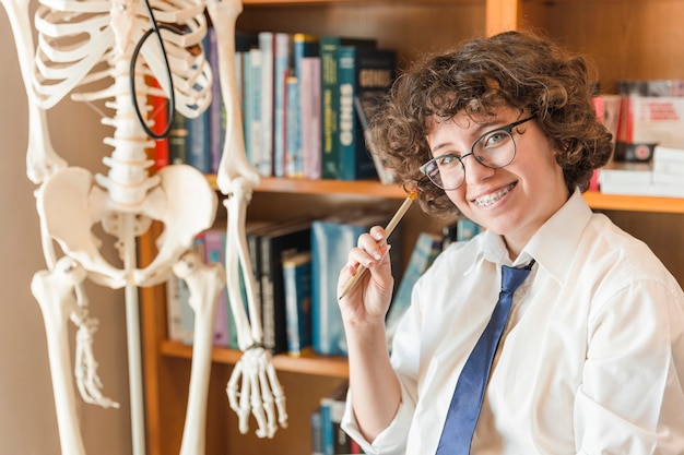 Cheerful teen girl sitting near skeleton model