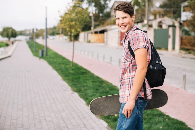 Cheerful teenager carrying skateboard