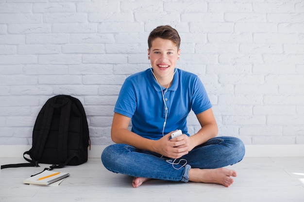 Free photo cheerful teenager listening to music on floor