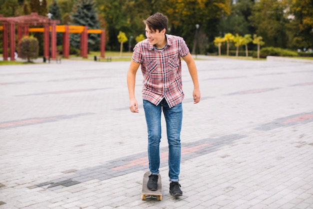 Cheerful teenager riding skateboard in park