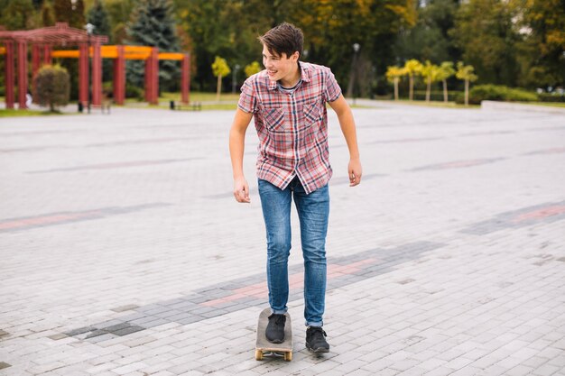 Веселый подросток катается на скейтборде в парке