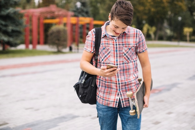 Foto gratuita adolescente allegro con smartphone e skateboard