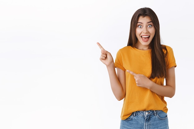 Cheerful, thrilled and amused cute girl taking part awesome giveaway want win trip abroad, pointing upper left corner, smiling amused and look excited camera, standing white background joyful