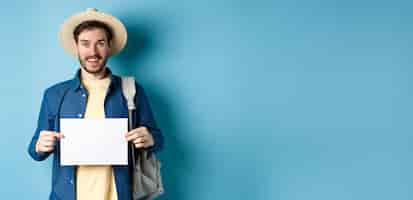 Free photo cheerful tourist in summer hat showing empty piece of paper and smiling hitchhiking with backpack st