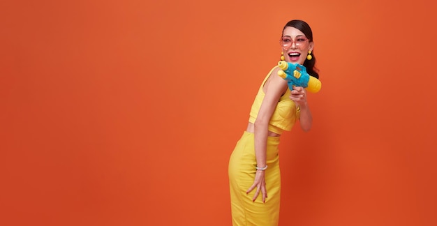 Cheerful tourist woman traveling with water gun during Songkran festival studio background