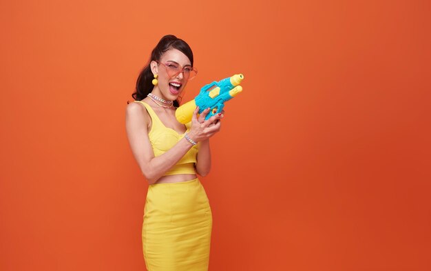 Cheerful tourist woman traveling with water gun during Songkran festival studio on background