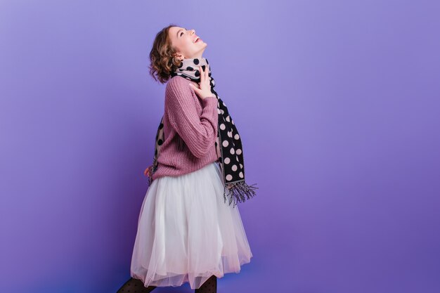 Cheerful trendy girl with long dark scarf posing in lush skirt posing  Photo of pretty female model with curly dark hair enjoying photoshoot.