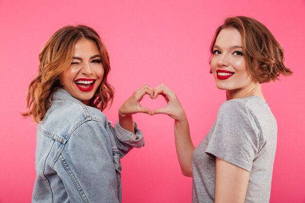 Cheerful two women hugging showing heart love gesture.