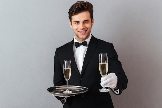 Free photo cheerful waiter holding glass of champagne give it to you.