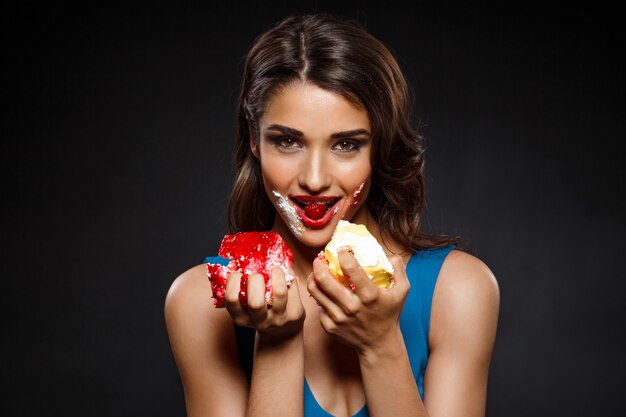 Cheerful woman in blue dress eating two pieces of cake