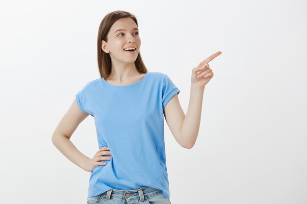 Cheerful woman in blue t-shirt pointing upper right corner, showing your logo