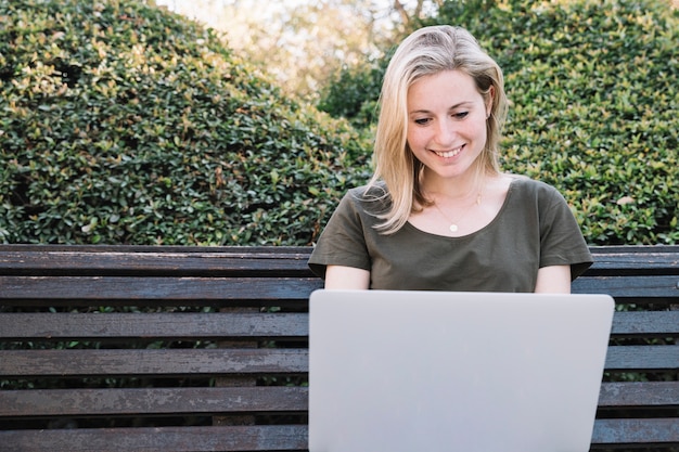 Cheerful woman browsing laptop on bench