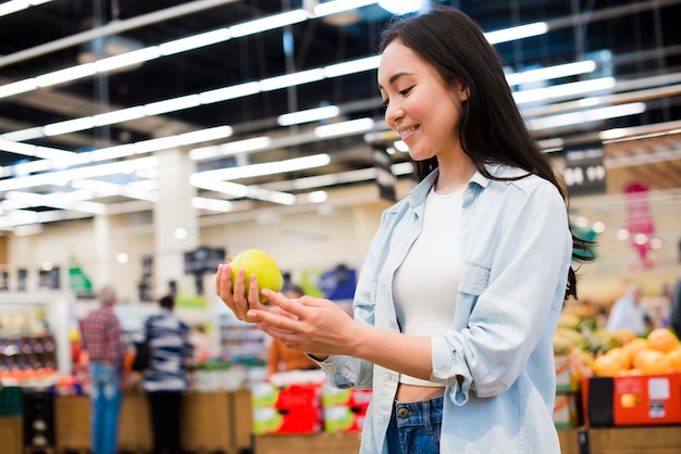 Cheerful woman checking apple in grocery store
