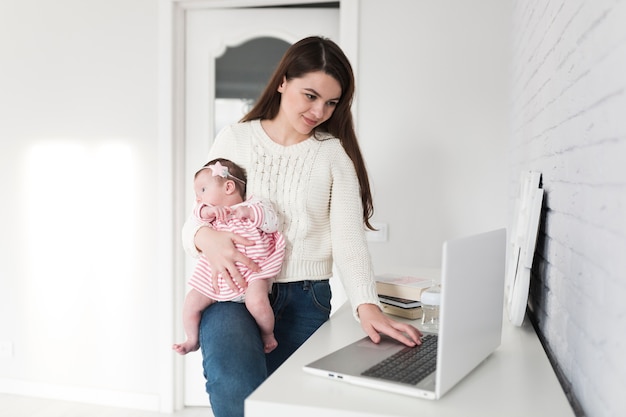 ラップトップをチェックして子供を運んでいる朗らかな女性