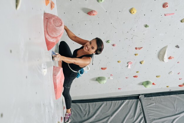 Cheerful woman climbing wall in gym