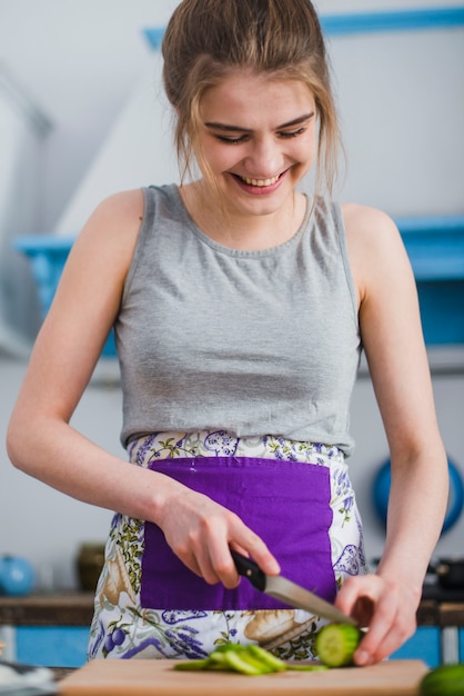 Cheerful woman cutting cucumber