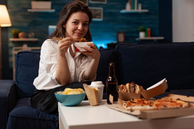 Веселая женщина ест вкусную китайскую еду, расслабляясь на диване