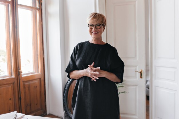 Cheerful woman in eyeglasses and dress posing in office