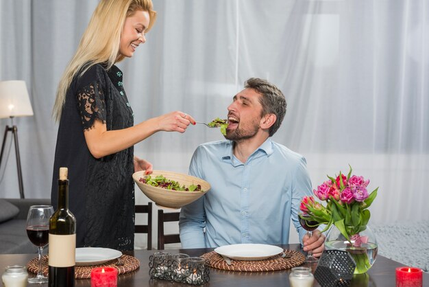 陽気な女性がテーブルで男にサラダを与える
