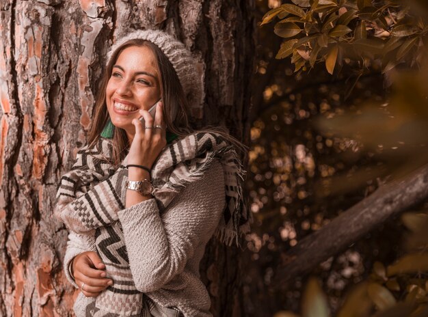 Веселая женщина с телефонным разговором возле дерева