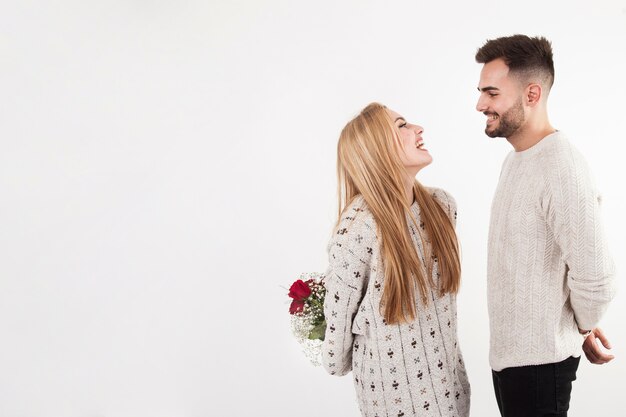 Cheerful woman hiding bouquet from man