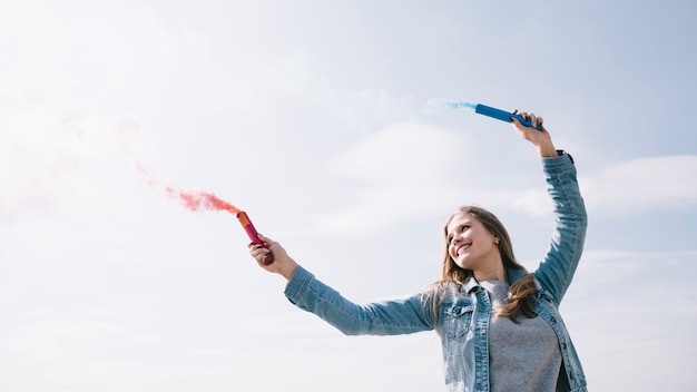 Cheerful woman holding smoke flares in outstretched hands