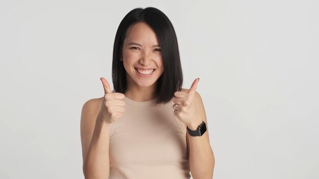 Cheerful woman keeping thumb raised showing her agreement over white background Female satisfying with something Like gesture