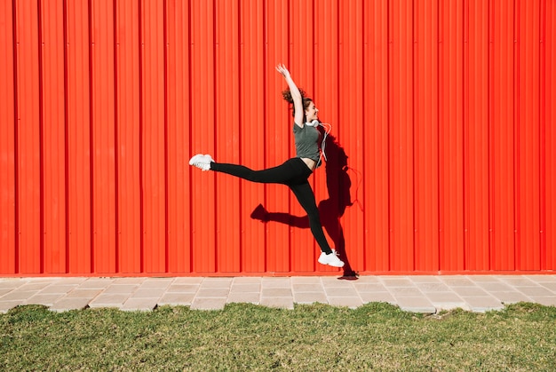 Cheerful woman leaping near red wall