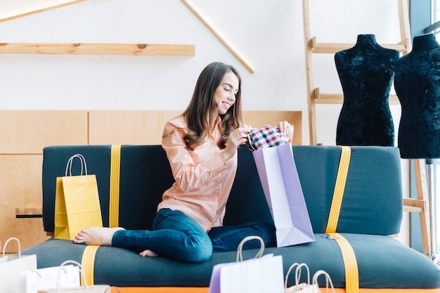 Free photo cheerful woman looking at purchases on sofa