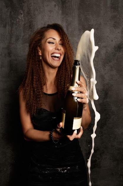 Веселая женщина открывает бутылку шампанского и веселится на вечеринке