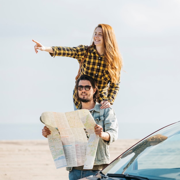 Cheerful woman pointing near man looking at map near car