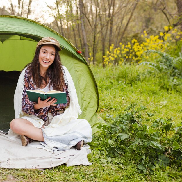 Cheerful woman reading book near tent