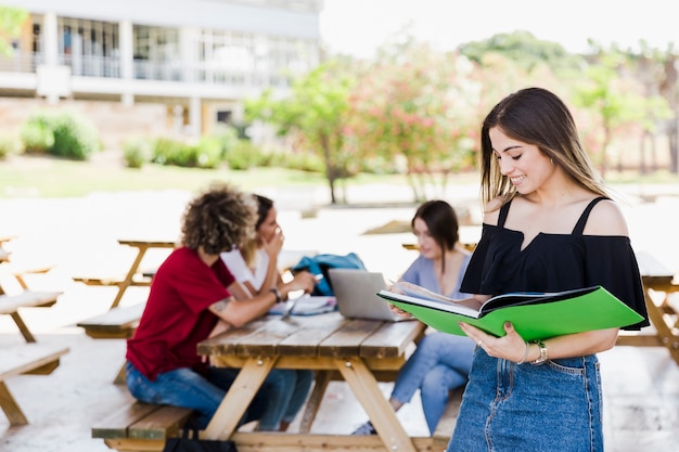 Cheerful woman reading textbook near friends