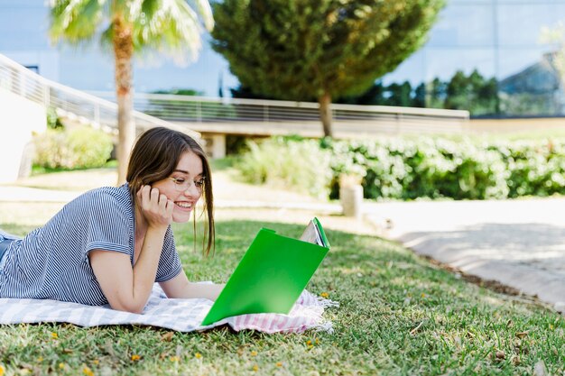 Cheerful woman reading textbook on park grass