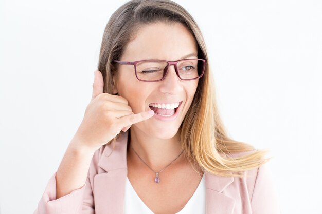 Cheerful woman showing call gesture and winking