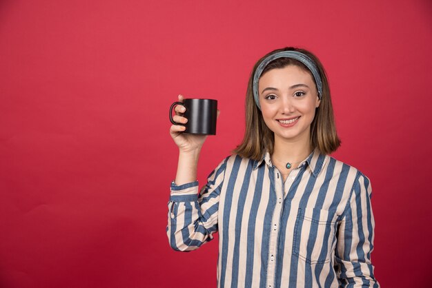 Cheerful woman showing cup of coffee and posing to front